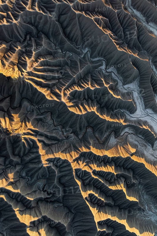 Aerial photo capturing golden desert textures and intricate patterns of Caineville Mesa, Utah. The sunlight casts dramatic shadows, highlighting the rugged terrain
