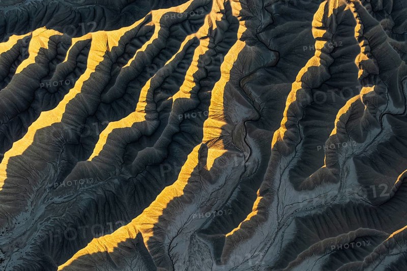 Aerial view of Caineville Mesa, Utah, showcasing dramatic ridges illuminated by golden sunlight. The textured landscape captures the essence of desert beauty and erosion