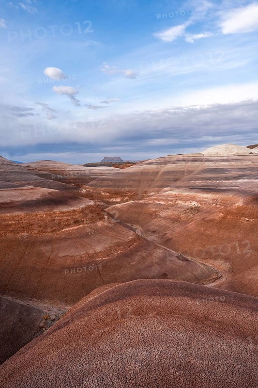 Panoramic view of Hanksville's bentonite hills in Utah, showcasing layers of vibrant earth tones under a vast blue sky, embodying the serene beauty of desert landscapes