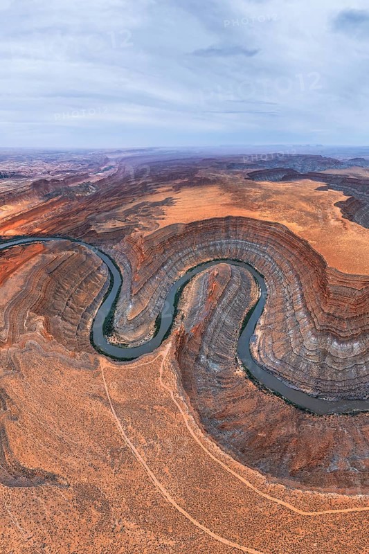 An aerial view captures a winding river cutting through a desert in San Juan canyon, showcasing layered rock formations and contrasting earth tones under an expansive sky in Utah, USA