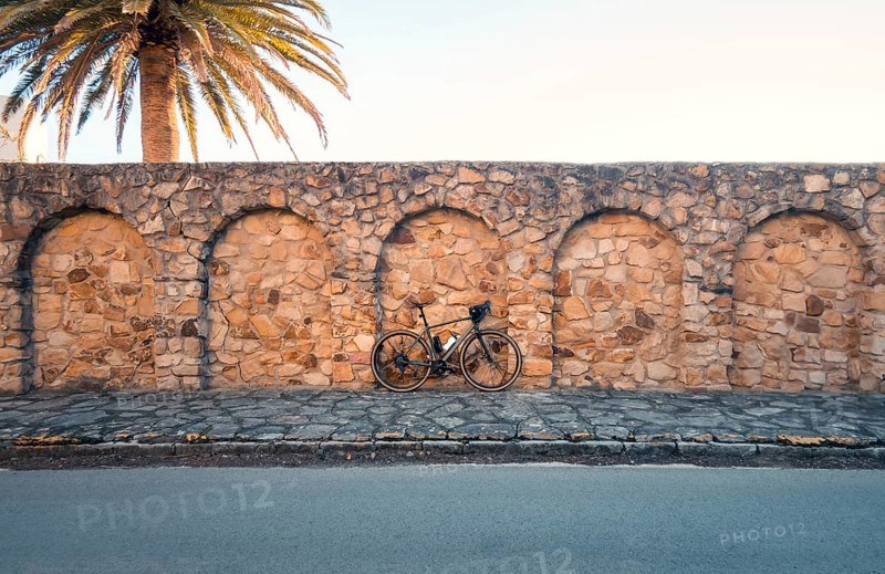 A bicycle leaning against an ancient stone wall under a palm tree, capturing the peaceful ambiance of Zahara de los Atunes, Cadiz