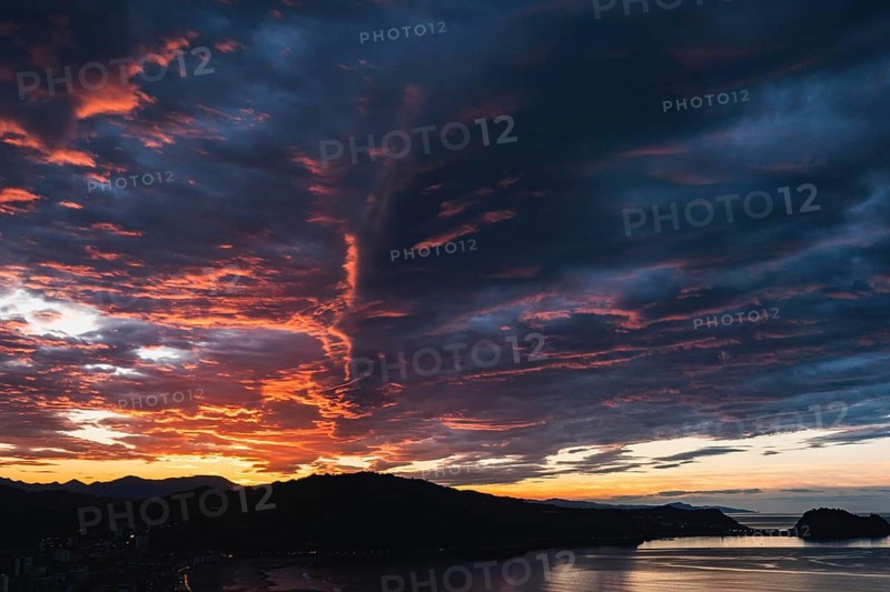 Breathtaking view of vibrant sunset skies above rolling hills framing a serene coastal backdrop, capturing the enchanting beauty of nature