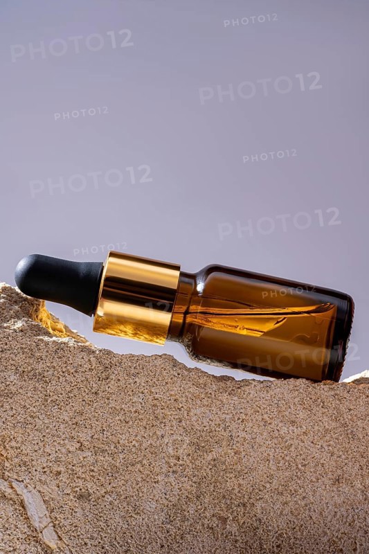 A high-angle shot of an elegant amber glass cosmetic dropper bottle elegantly placed on a textured stone podium, emphasizing luxury and natural beauty. Ideal for showcasing sophisticated skincare products