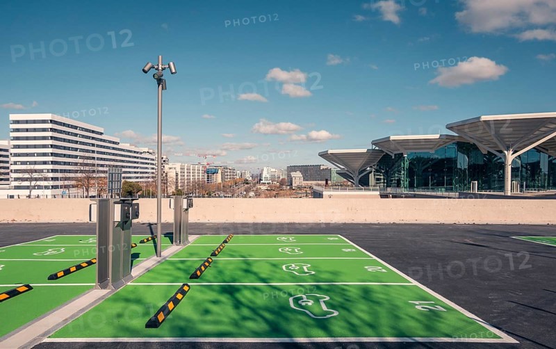 A newly constructed transport hub in Valdebebas, Madrid, featuring a sleek glass facade and modern design. Facilities for metro, underground, suburban trains, and buses. Equipped with a spacious green parking area for electric vehicles
