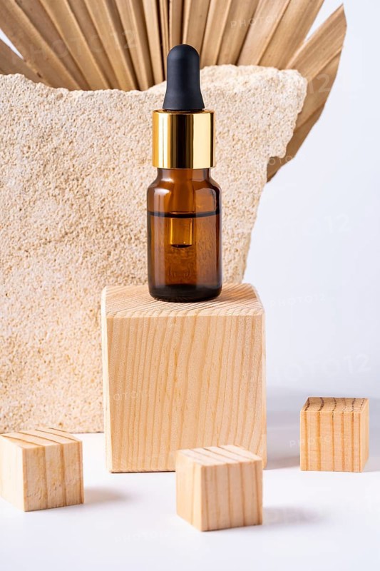 A premium cosmetic dropper bottle displayed on a wooden podium, accompanied by smaller wooden blocks, against a textured stone background