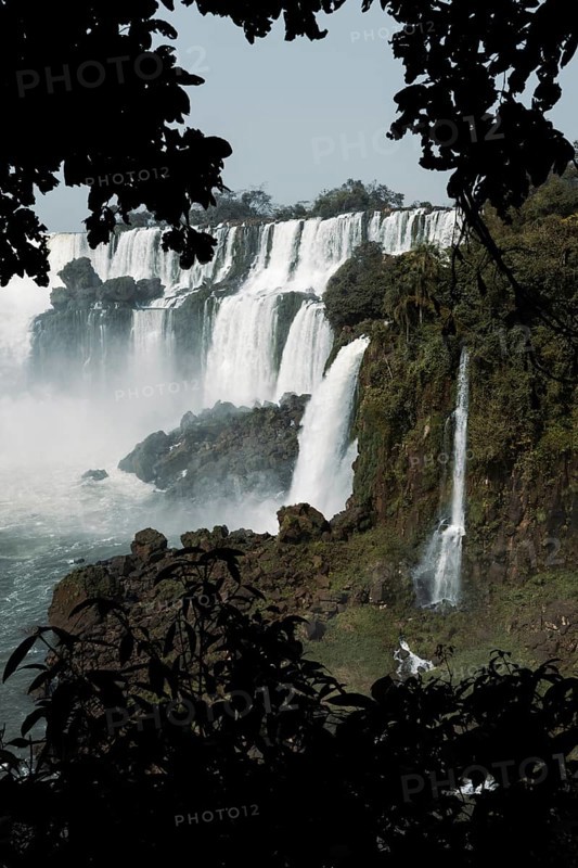 Captivating photo of Iguazu Falls framed by dark foliage, showcasing multiple cascades amid verdant nature