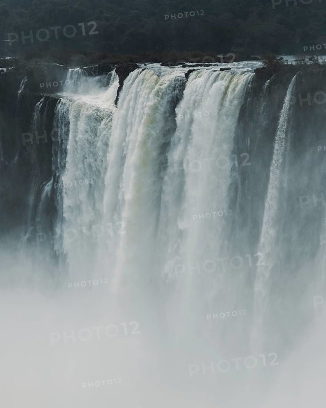 Mist surrounds the powerful, cascading waters of Iguazu Falls located on the border of Argentina and Brazil. The dense fog enhances the mystical appearance of the falls, adding a sense of awe to the natural scenery