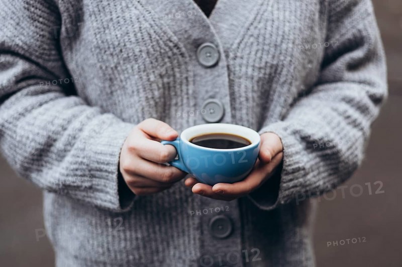 A person in a cozy gray sweater holds a blue cup coffee, capturing a peaceful moment of warmth and comfort, perfect for a chilly day