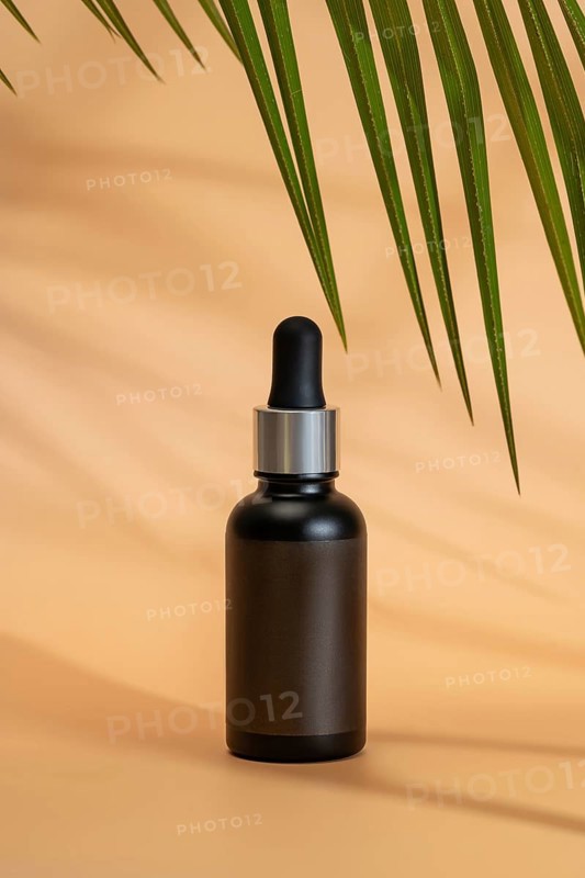 Black cosmetic dropper bottle on a beige background, with palm leaf shadows. The minimalist, tropical theme highlights the product, perfect for skincare branding