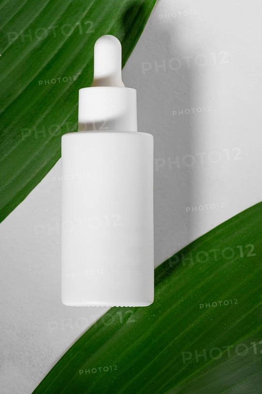 Minimalist presentation of a white dropper bottle lying on vibrant green leaves, highlighting its eco-friendly and natural appeal