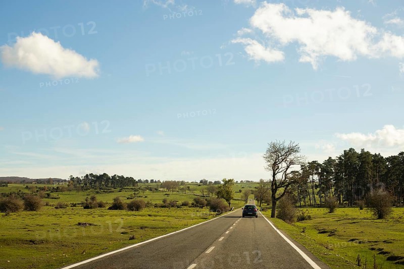 A car travels along a quiet country road under a clear blue sky on a peaceful autumn morning The landscape features lush green fields and scattered trees