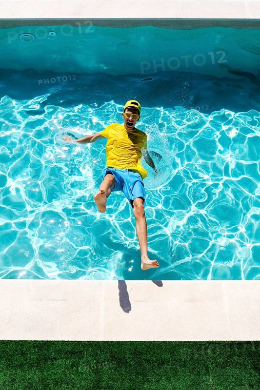 A joyful person in a colorful outfit splashes into a clear blue pool on a sunny day, expressing fun and energy. The vibrant water and lively scene evoke summer enjoyment