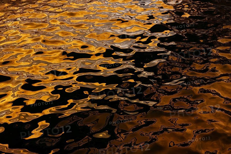 Artistic close-up of shimmering water reflecting golden hues under sunlight at Playa Blanca Port, Lanzarote, capturing the mesmerizing patterns formed