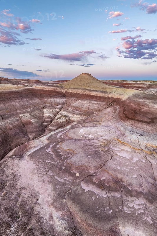 A breathtaking aerial photo captures the unique geological formations of bentonite clay in Utah, showcasing a spectrum of earthy colors and intricate patterns against a backdrop of soft pink clouds at dusk