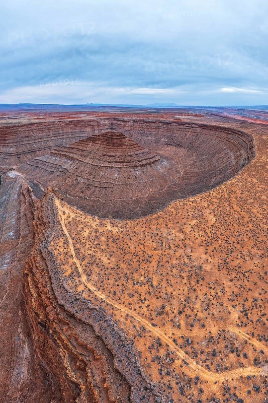 A breathtaking aerial view captures the intricate layers of a desert in San Juan canyon, showcasing winding paths and geological formations under a vast, cloudy sky in Utah, USA