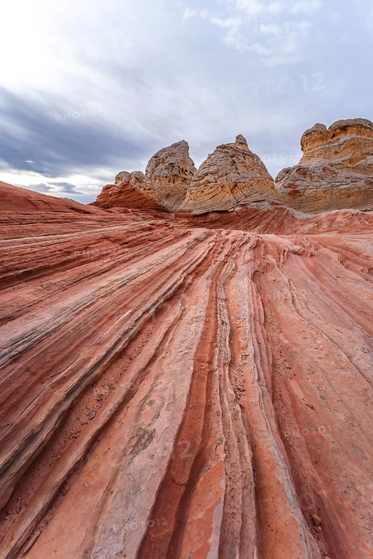 Vibrant and textured red rock formations stretch under a cloudy sky at White Pocket in Arizona, USA, showcasing nature's artistry in stone