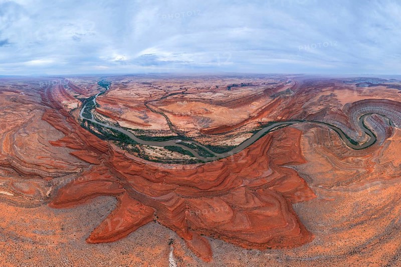 A breathtaking aerial view of a desert landscape. A winding river cuts through red rock San Juan canyons under a vast, cloudy sky, showcasing nature beauty and grandeur of Utah, USA
