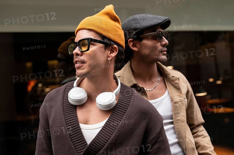 A Colombian gay couple enjoying a relaxed moment together. They wear fashionable clothes, sunglasses, and hats, sitting closely with a sense of camaraderie and warmth