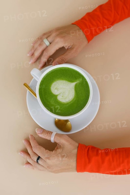 A woman enjoys a matcha latte in a Warsaw cafe Her vibrant orange clothing and trendy rings add flair to the serene setting, showcasing contemporary lifestyle