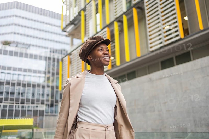 A fashionable black woman walks through an urban area, surrounded by contemporary architecture Her confident smile complements the city's vibrant atmosphere