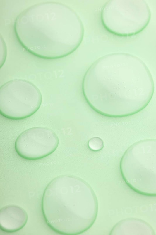 This image features a close-up view of translucent droplets scattered on a smooth, light green surface The droplets vary in size, creating a fresh and calming atmosphere