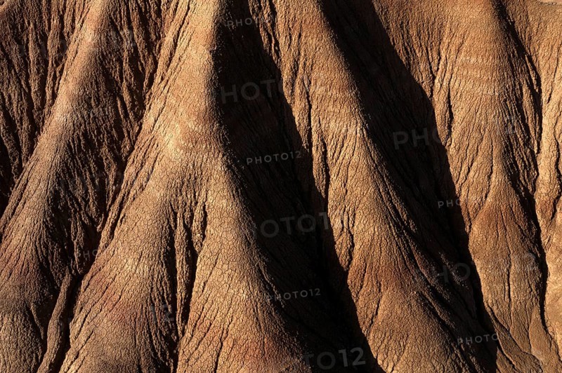 Aerial view of a rugged desert landscape showcasing intricate erosion patterns and ridges in brown tones, capturing the stark beauty of arid terrain and natural formations