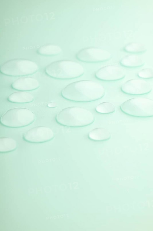 Droplets scattered on a smooth mint green surface, creating a calming and refreshing scene Soft lighting enhances the translucent texture, evoking tranquility and purity