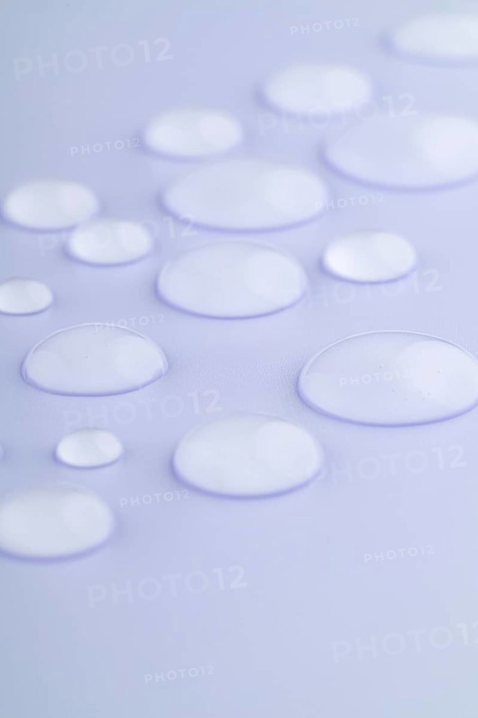 Close-up image of droplets scattered on a smooth, lavender-colored surface The droplets vary in size, creating a calming and serene visual effect