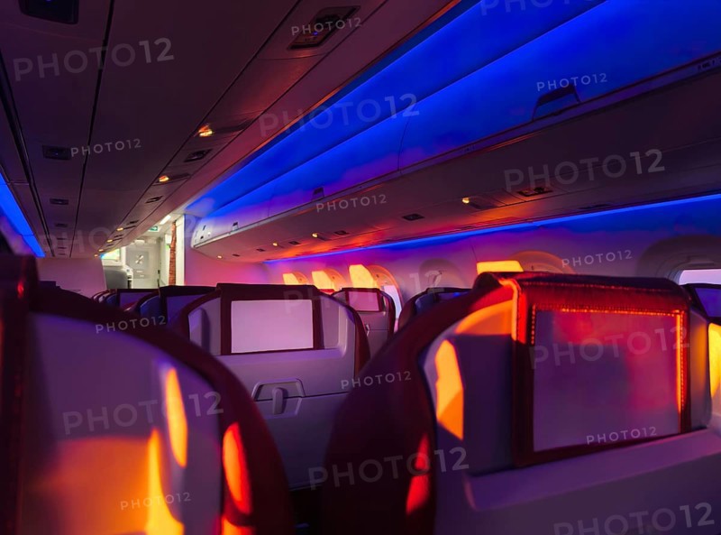 Interior view of an airplane cabin aglow with vibrant mood lighting, showcasing the comfortable seating and modern ambiance during a nighttime flight