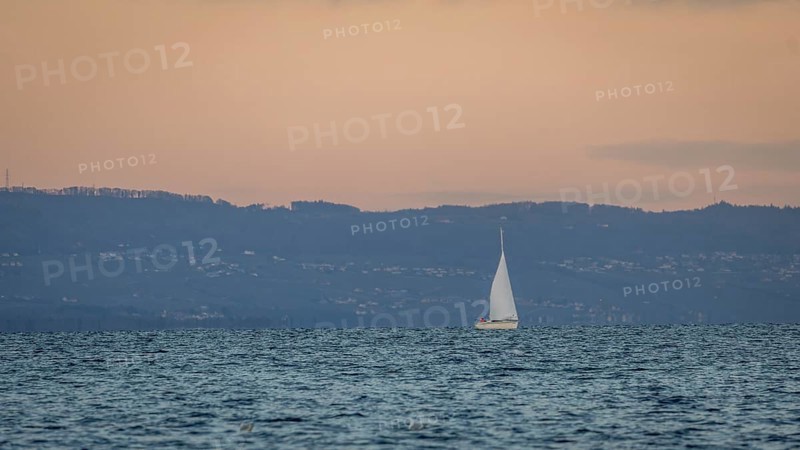 A serene scene of a sailboat gracefully moving across a calm lake in Geneva, set against a backdrop of distant hills during a tranquil sunset, creating a peaceful atmosphere