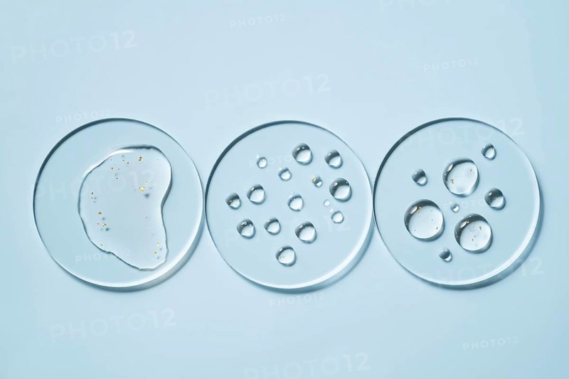Three transparent petri dishes with water droplets placed on a light blue surface The circular arrangements create a minimalist and scientific aesthetic