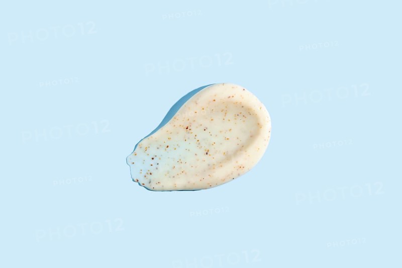 A dab of exfoliating cream with visible scrub particles smeared on a pastel blue background showcasing the texture of skincare products