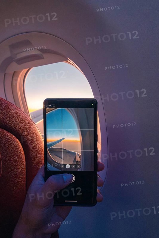 Cropped unrecognizable person capturing a serene sunset through an airplane window using a smartphone, highlighting the use of technology to record beautiful moments mid-flight