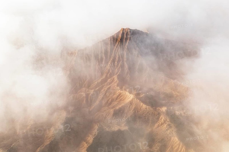 A breathtaking mountain peak emerges through a dense layer of clouds, showcasing its rugged terrain The soft, swirling mist adds an ethereal touch to the scene, enhancing its majestic beauty