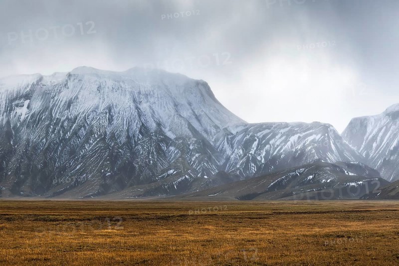 Captivating landscape of the Icelandic Highlands featuring rugged, snow-capped mountains under cloudy skies. Vast open plains stretch in the foreground, conveying solitude and grandeur