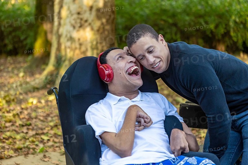Heartwarming image of Spanish Cameroonian siblings outdoors, one in a wheelchair with cerebral palsy. Their mixed-race heritage adds a rich layer to their joyful bond