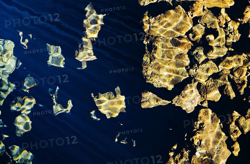 Sunlight reflecting on water, illuminating rocks below. The combination of light and texture creates a golden abstract scene
