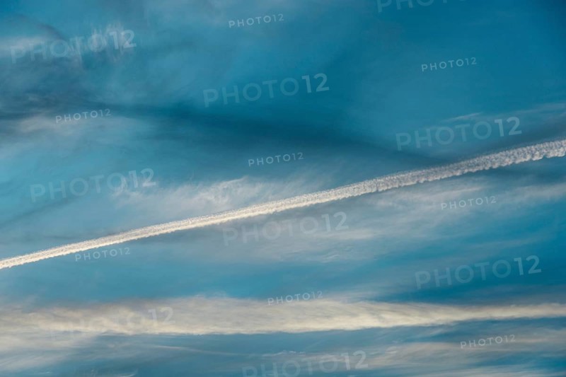Airplane contrail across a clear blue sky. The white streak contrasts beautifully with the soft clouds in the background
