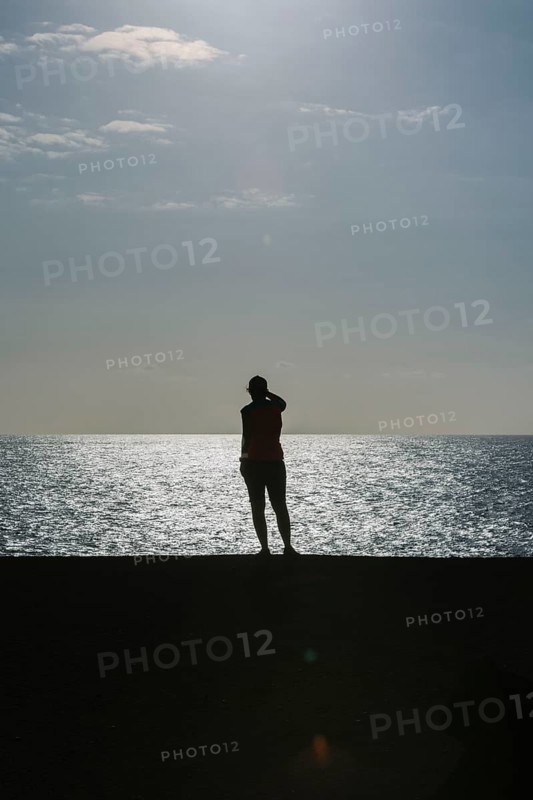 Silhouette of a person standing by the sea during sunset. The calm water and warm light create a peaceful atmosphere