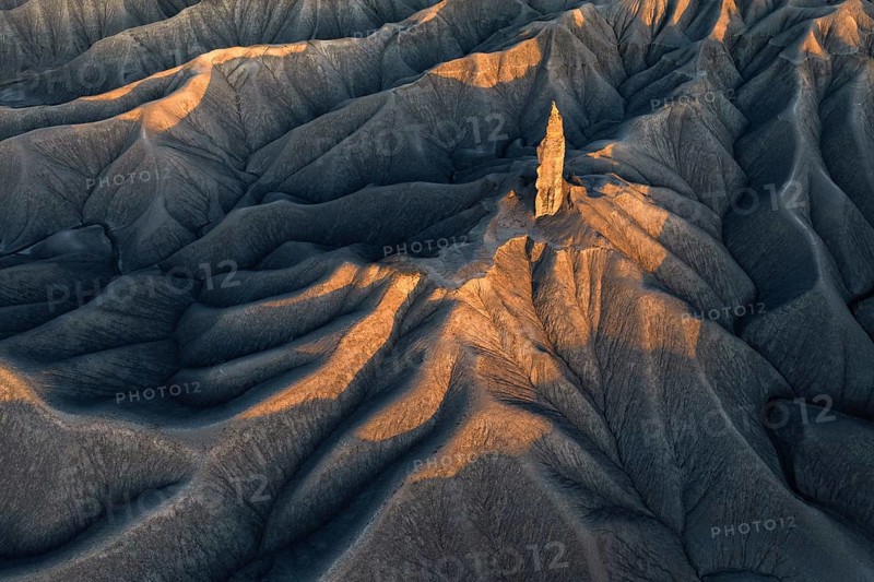 A striking aerial view of the textured terrain of Caineville Mesa near Hanksville, Utah, bathed in the warm golden light of the setting sun, highlighting the unique geological formations