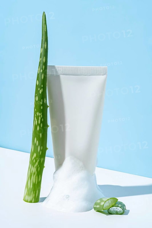 A white tube of cosmetics cream squeezed to show its contents, alongside an aloe vera plant, symbolizing natural skincare ingredients