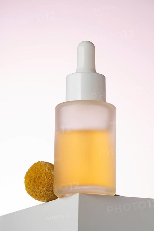 Elegantly displayed cosmetic serum bottle with a dropper, positioned on a geometric podium against a soft pink background, highlighting the product's sleek design and premium quality