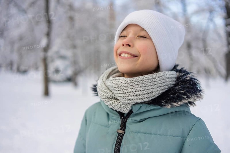 A young girl stands amidst a snowy landscape, wearing a warm scarf and hat, radiating happiness. The winter scene in the background adds to the serene atmosphere