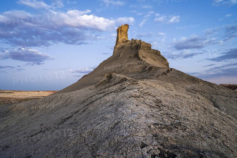 This image captures a striking rock formation in the deserts of Utah, USA, highlighted by a dynamic cloudy sky above and rugged terrain beneath, illustrating the area's natural beauty and geological diversity