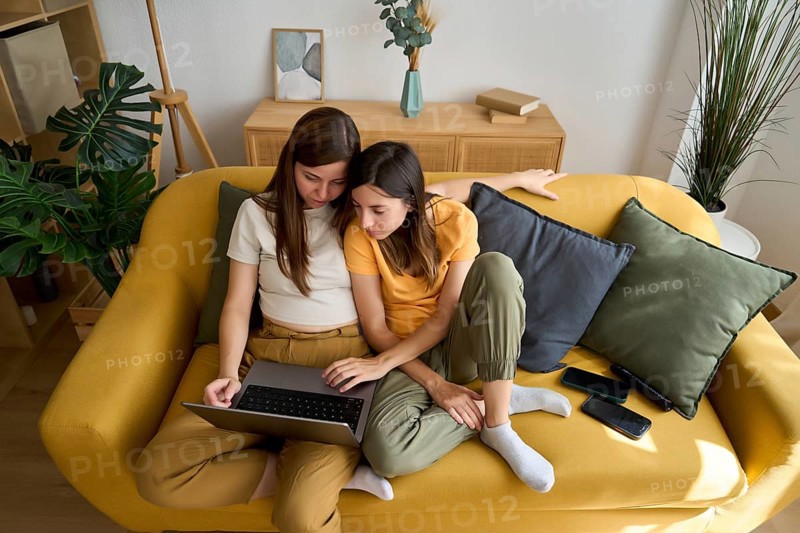A warm scene captures a lesbian couple sharing a laptop on a cozy couch They seem comfortable and content, enjoying a quiet moment together in their stylish living room