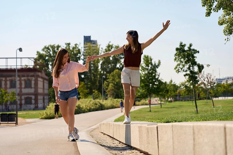 A joyful lesbian couple enjoys a sunny day, holding hands and balancing on a sidewalk in a park, embracing love and freedom Perfect representation of LGBTQIA+ pride