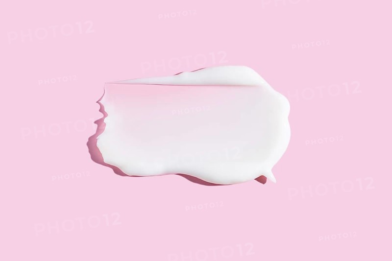 A dollop of white cream or gel cosmetic product smeared on a pastel pink background, depicting a rich and smooth texture