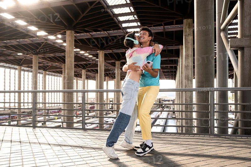 A joyful moment for a couple embracing each other at a train station. The sunlight filters through the architectural supports, highlighting their happiness