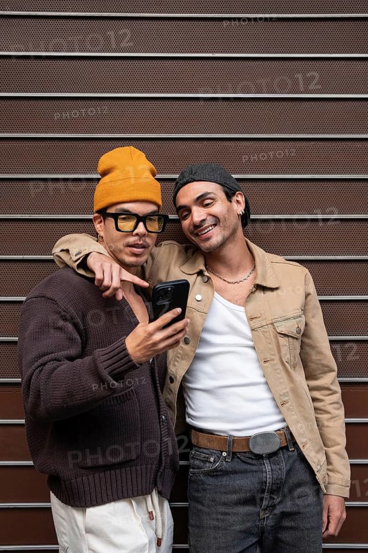 A joyful couple stands close together, sharing a moment and viewing something exciting on a smartphone. Their casual attire and warm smiles exude happiness and connection