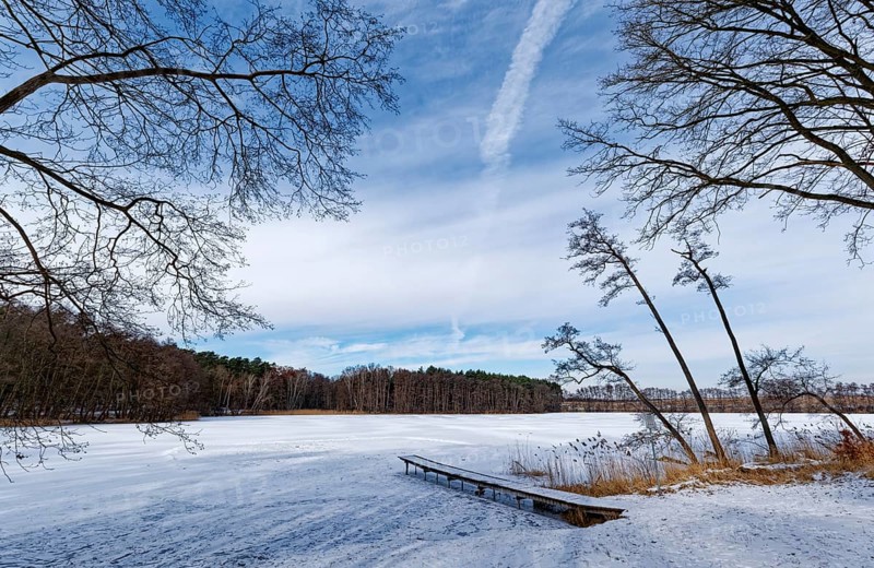 Winter day at the swimming area and jetty on the snow-covered Heiliger See, a lake in the Grumsin Beech Forest UNESCO World Heritage Site, part of the UNESCO Schorfheide-Chrorin Biosphere Reserve. Altkünkendorf, Angermünde, Uckermark, Brandenburg, Germany